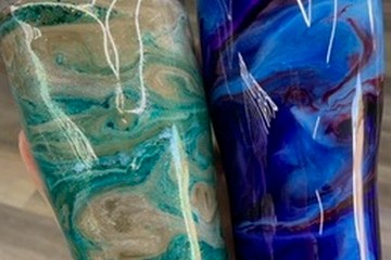 Hand holding two marbled tumblers in green and blue.