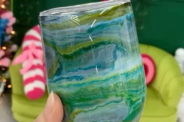 Hand holding a marbled blue-green tumbler in a colorful room with 'Be Creative' neon sign.