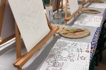 Easels with blank canvases set up on a table with painting supplies and coloring activity sheets.