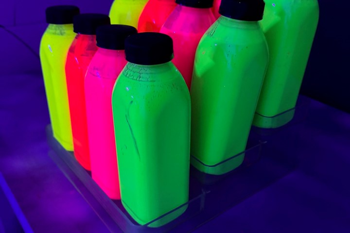Bright neon bottles glowing under blacklight on a table.